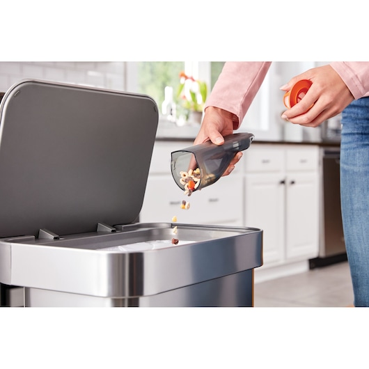 BLACKDECKER HLVC315J11 handheld vacuum dustbin being emptied into a kitchen trash can.