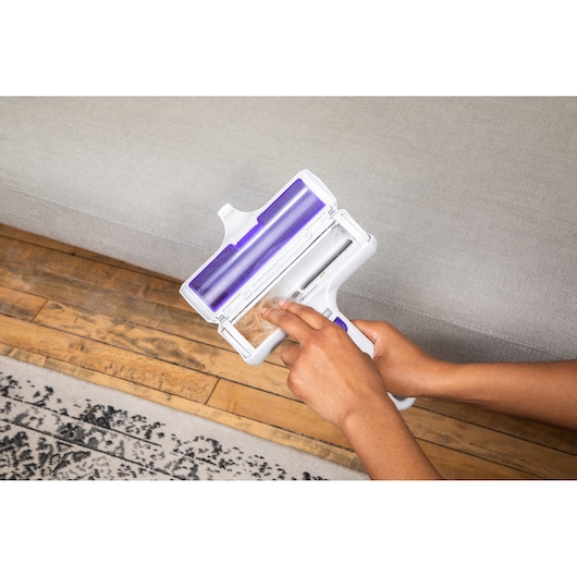 BLACKDECKER HMSCT0001 handheld lint remover in use on light gray upholstery.