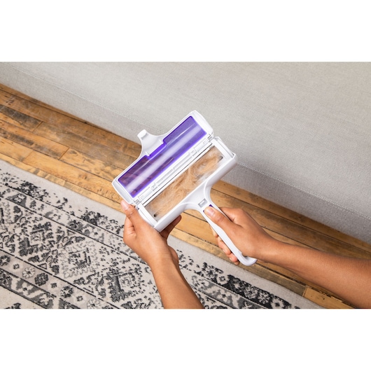 BLACKDECKER HMSCT0001 pet hair remover being held near a sofa and rug, open to show collected hair.