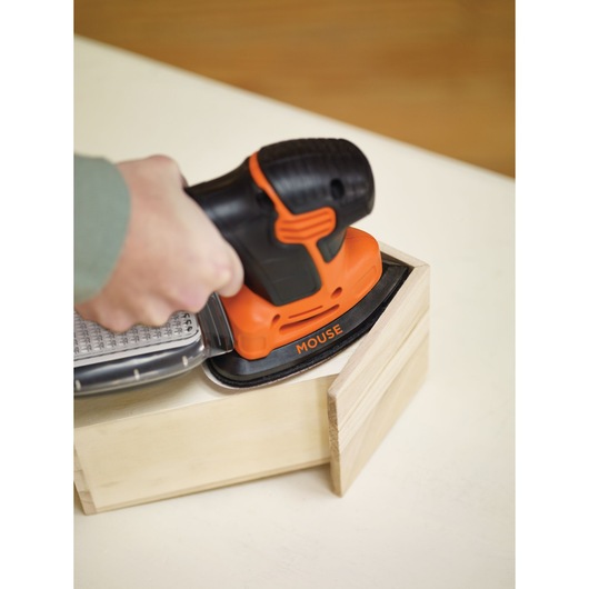 BLACKDECKER KA2000KA10 orange and black mouse sander in use on a wooden box, close-up angle.