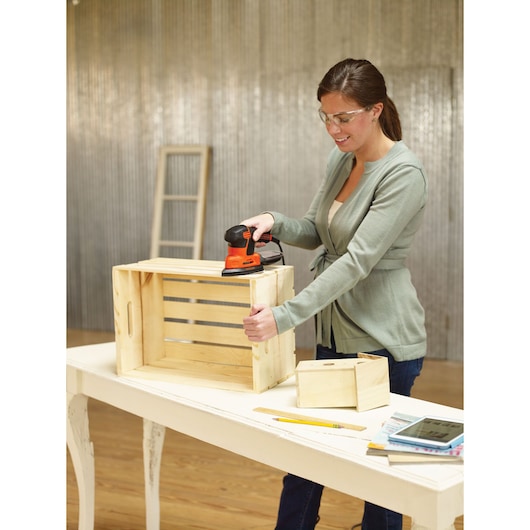 BLACKDECKER KA2000KA10 sander used on a wooden crate, table with tools, indoor workshop setting.