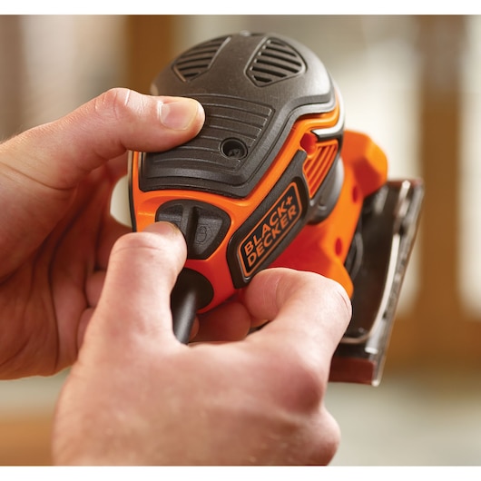 Close-up photo of BLACK+DECKER KA450 detail sander being operated by hand, orange and black body visible.