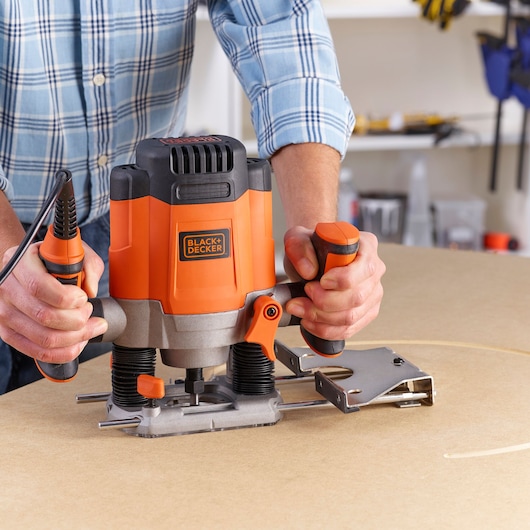 BLACKDECKER KW1200E plunge router in use on a wooden surface, orange and black design, workshop background.