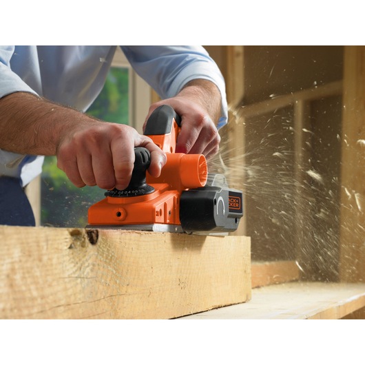 BLACKDECKER KW750K electric planer in use on wood, close-up action shot, orange and black tool with handle.