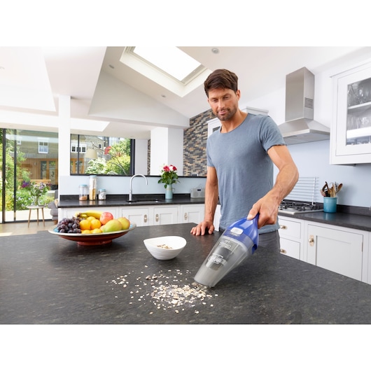 BLACK+DECKER NVC115WA handheld vacuum cleaning crumbs on kitchen counter near fruit bowl.
