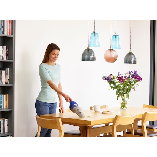 BLACKDECKER NVC115WA handheld vacuum used to clean crumbs from a wooden dining table in a modern kitchen.
