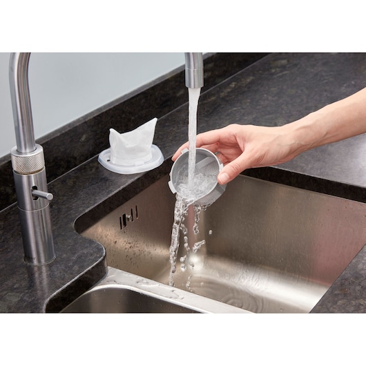 BLACKDECKER NVC115WA filter being rinsed under running water in a kitchen sink, close-up angle.
