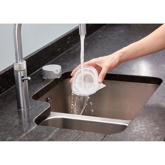 BLACK+DECKER NVC115WA vacuum filter being rinsed under faucet in kitchen sink.