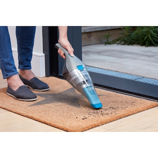 BLACKDECKER NVC215WA handheld vacuum cleaning dirt from doormat indoors.