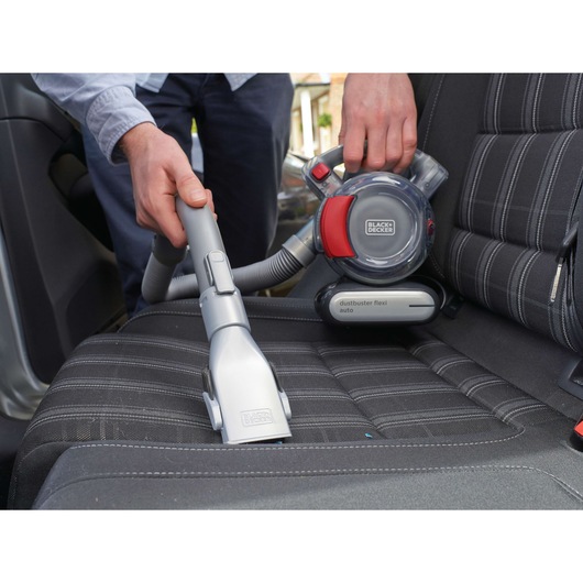 BLACKDECKER PD1200AV handheld vacuum cleaning a car seat, close-up of nozzle and flexible hose.