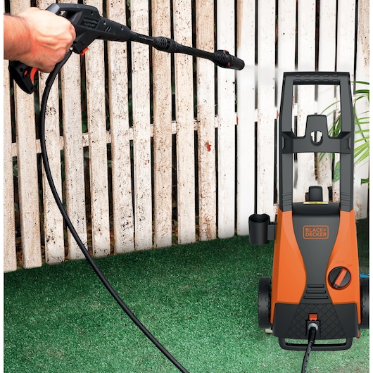 BLACKDECKER PW1450TDL pressure washer cleaning a white fence outdoors.