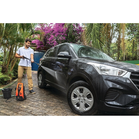 BLACKDECKER PW1450TD pressure washer cleaning a black SUV outdoors near tropical plants.