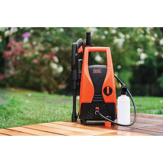 BLACKDECKER PW1450TD pressure washer in orange and black with accessories on outdoor patio.