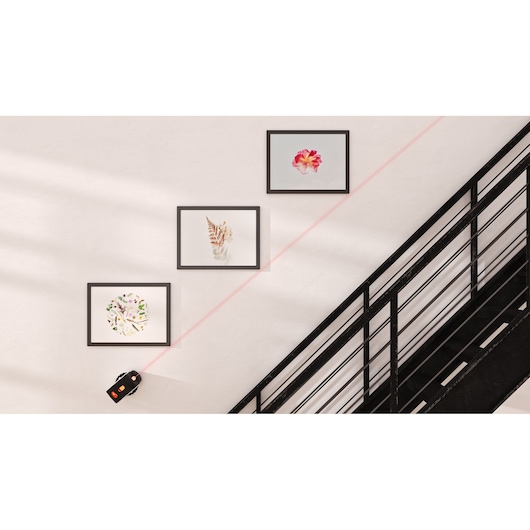 Photo of BLACKDECKER REVBDLL100 laser level projecting a red line on a wall with three framed pictures near a staircase.