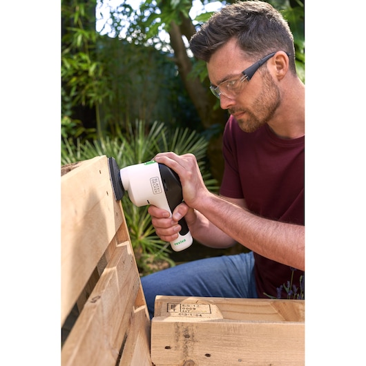 BLACK+DECKER REVDS12C sander being used on a wooden pallet outdoors.