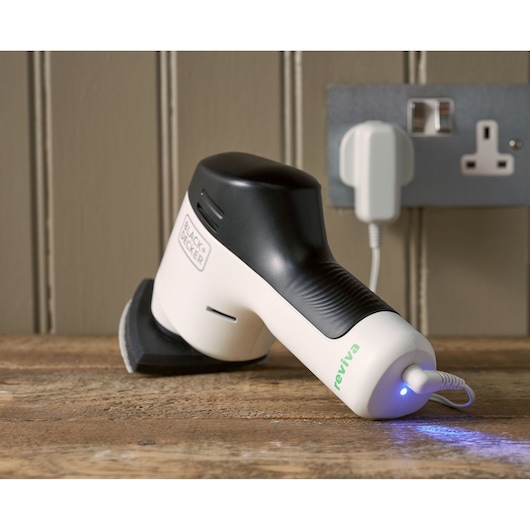 BLACK+DECKER REVDS12C compact white and black cordless sander charging on wood surface.