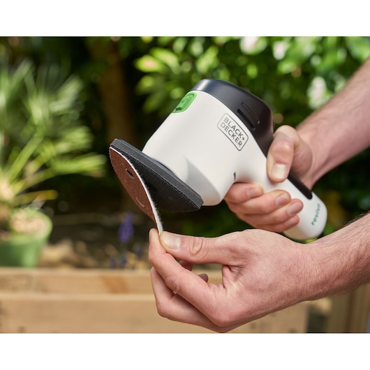 BLACKDECKER REVDS12C cordless detail sander in hand, close-up outdoors, person attaching sanding pad.