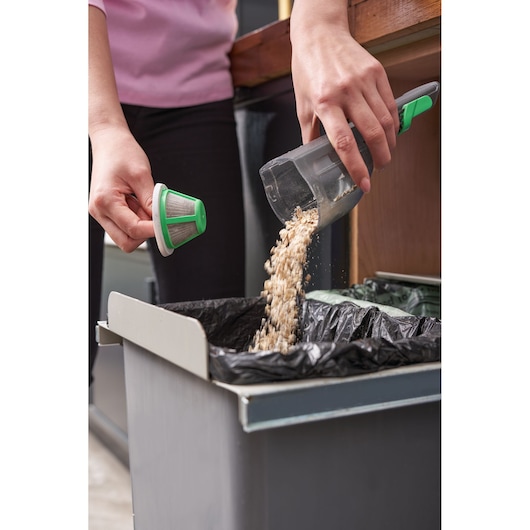 BLACKDECKER REVHV8C handheld vacuum being emptied into trash bin, person holding filter and waste container.
