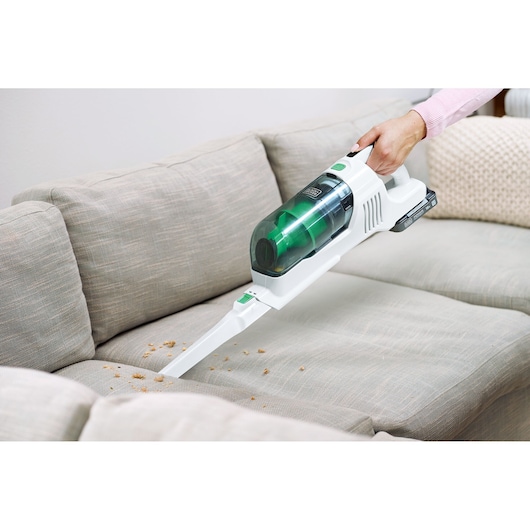 BLACKDECKER REVSV18D1 handheld vacuum with green accents cleaning sofa crumbs, side view.