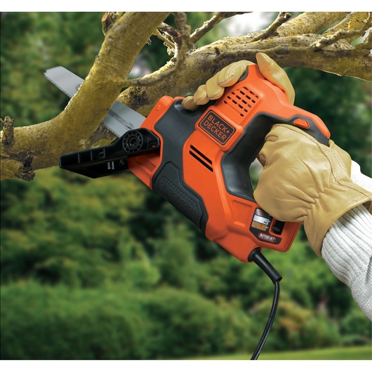 Photo of BLACK+DECKER RS890K orange and black electric saw cutting a tree branch outdoors, operated by gloved hands.