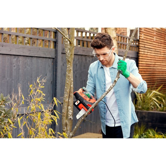 Person using BLACKDECKER RS890K electric saw to cut tree branch in a garden.
