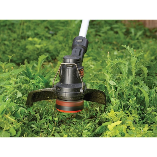 BLACKDECKER ST182320 grass trimmer head cutting green weeds outdoors.