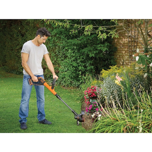 BLACKDECKER STC1820EPC grass trimmer in use trimming garden edge on green lawn.