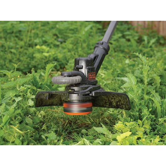 BLACKDECKER STC1820EPC grass trimmer in use, close-up on cutting head trimming green plants outdoors.