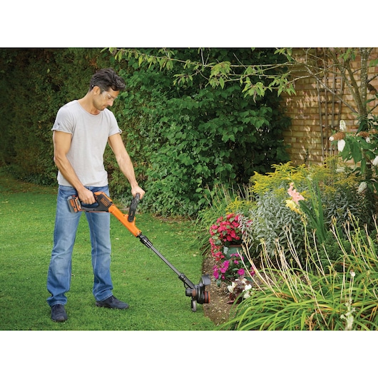 BLACKDECKER STC1840EPC grass trimmer used to edge lawn beside flowerbed outdoors.