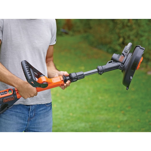 Photo of a person holding a BLACK+DECKER STC1840EPC cordless grass trimmer in a garden.