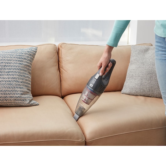 BLACKDECKER SVB620JW handheld vacuum cleaning beige sofa cushions in living room.