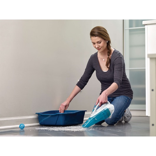 BLACKDECKER WDA315J handheld vacuum cleaning spilled litter near blue tray on tile floor.