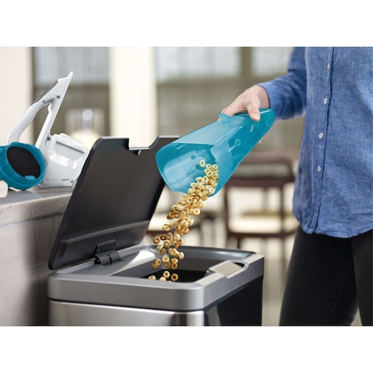 BLACKDECKER WDA315J handheld vacuum canister with cereal being emptied into trash bin, side angle