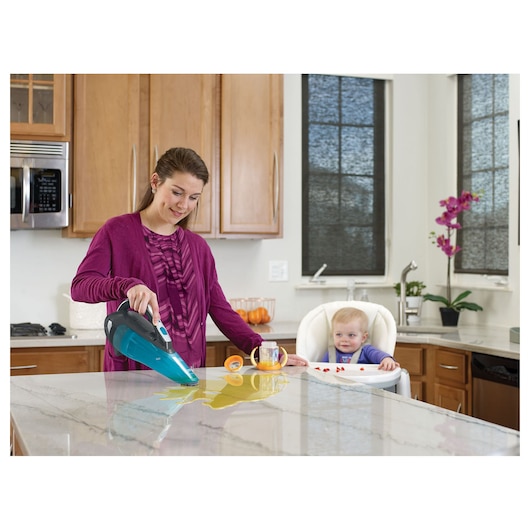 BLACK+DECKER WDA320J handheld vacuum cleaning spilled liquid on kitchen counter, baby sitting in high chair nearby.