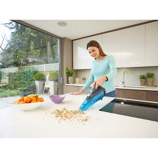 Photo of BLACKDECKER WDA320J handheld vacuum cleaning crumbs on a kitchen countertop.
