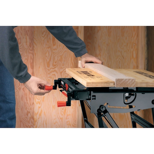 BLACKDECKER WM825 workbench with wooden board held in place, person adjusting clamp handle.