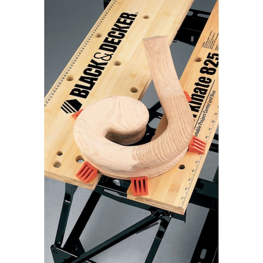 BLACK+DECKER WM825 workbench with wooden piece and orange clamps, top view on white background.